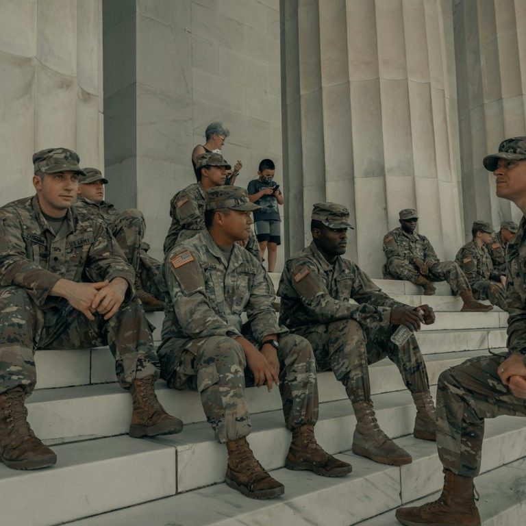 Soldiers in uniform sitting on steps, with children and others in the background.