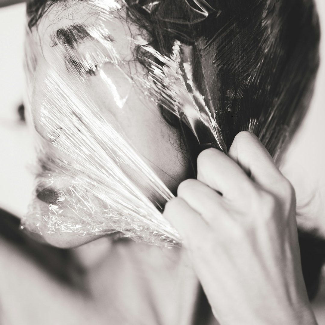 Person partially wrapped in clear plastic, touching their face with one hand.