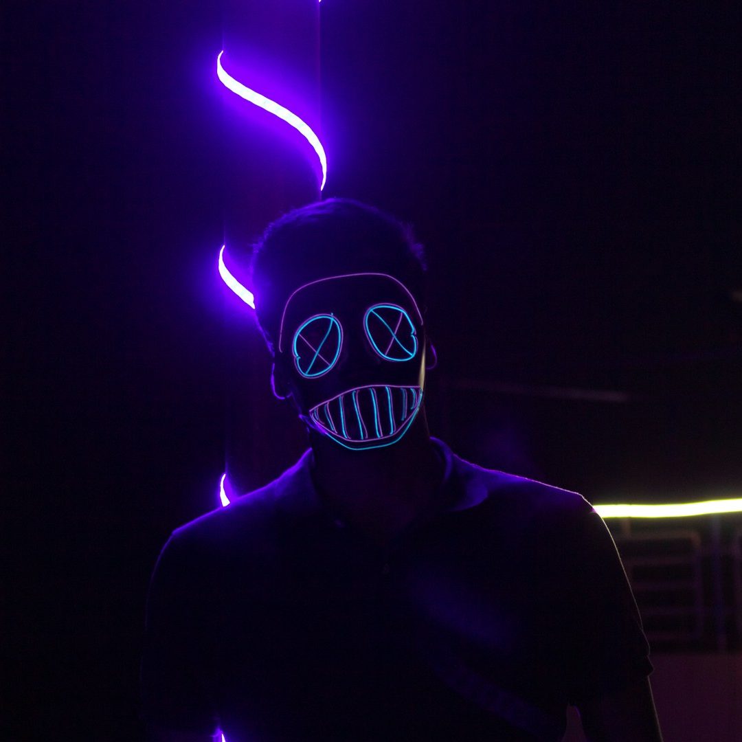 A person wearing a glowing mask with skull features against a dark background.