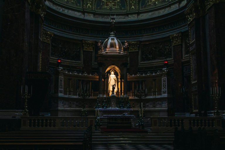 Statue illuminated in a dark, ornate hall with intricate details and a grand ceiling.
