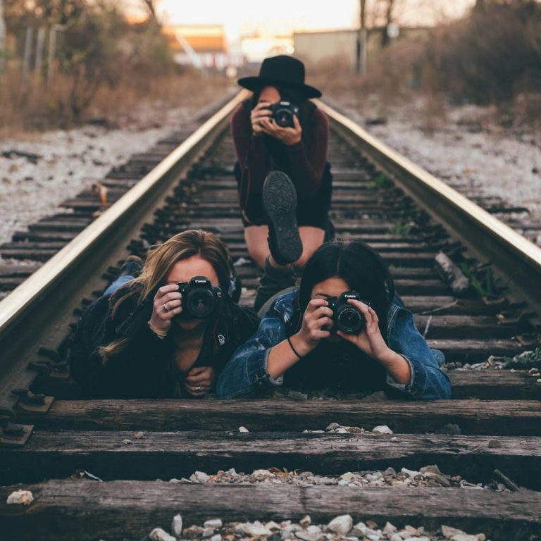 Three individuals lying on train tracks, each holding a camera and taking photos.