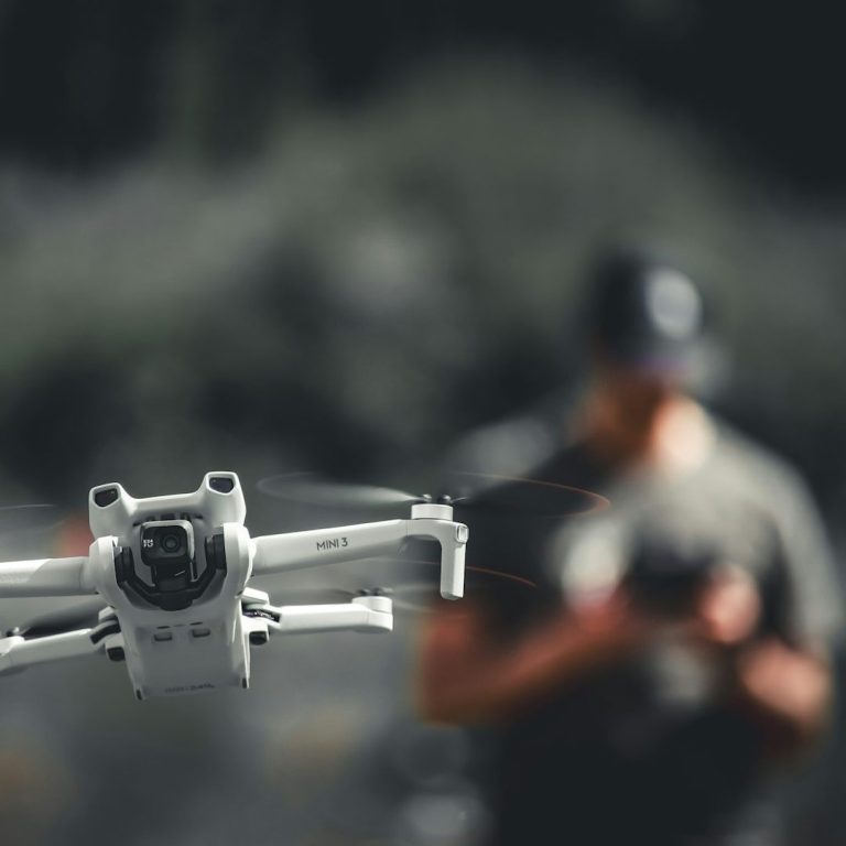 A close-up of a drone with a blurred person in the background holding a controller.