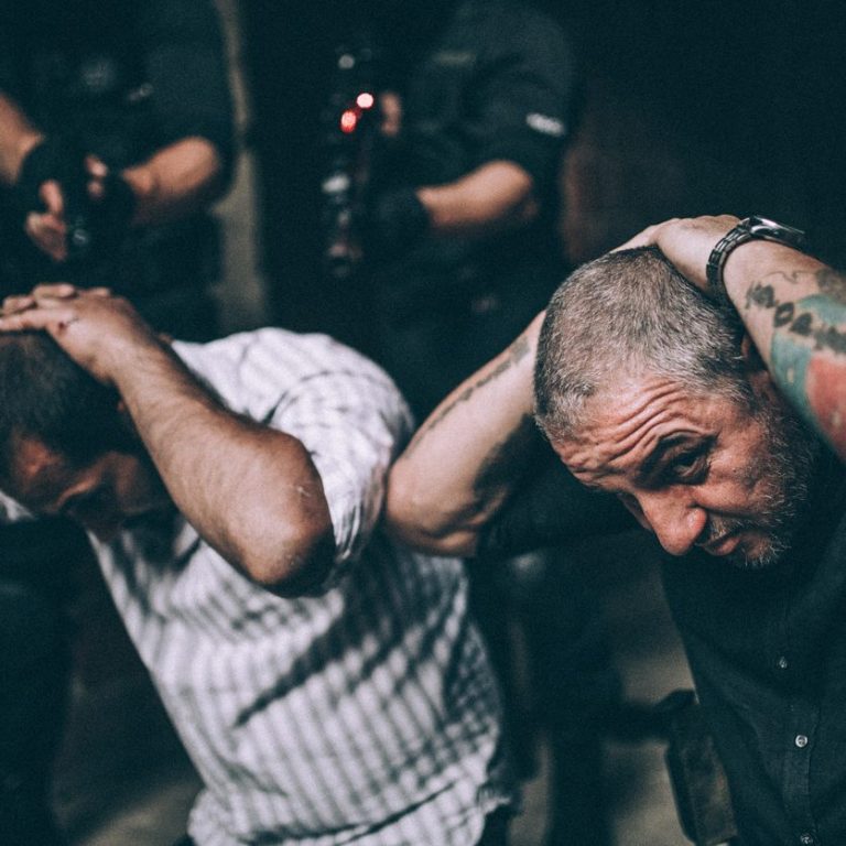PITC Module 2 Two men with shaved heads are being apprehended by armed officers in a tense situation.