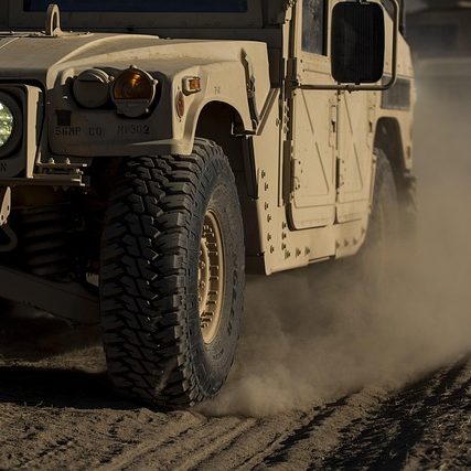 Military vehicle kicking up dust on a dirt road.