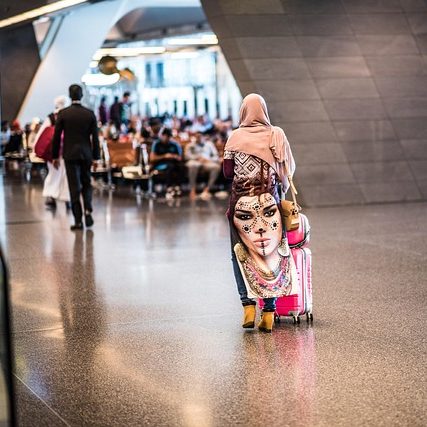 A woman in a hijab with a colorful bag walks with a child in a busy terminal.