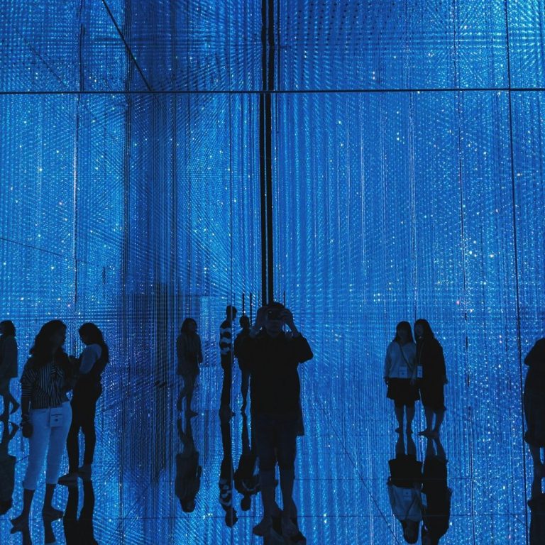 Silhouettes of people against a bright blue backdrop with shimmering lights.