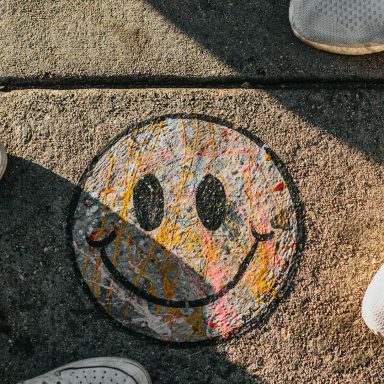 Colorful smiley face graffiti on pavement, surrounded by shoes.