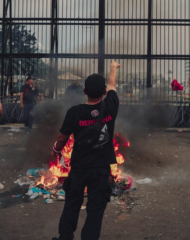 Two armed officers in tactical gear apprehend a restrained man in an indoor setting.