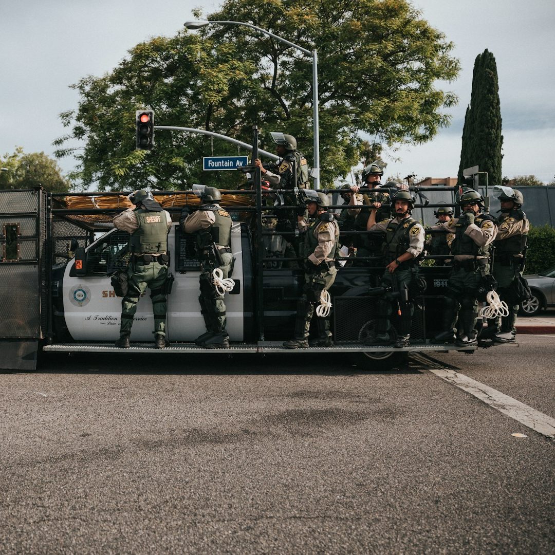 Police officers in tactical gear on a modified vehicle at an intersection.