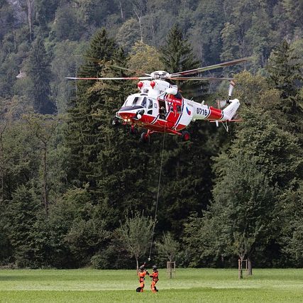 Rescue helicopter hovering above a person, surrounded by trees and open field.
