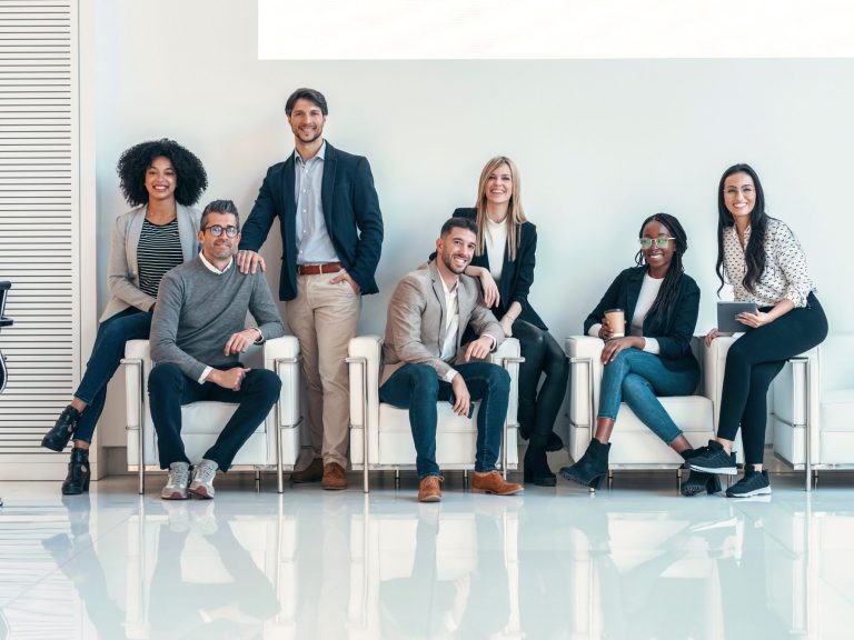 A diverse group of seven professionals posing together in a modern office environment.