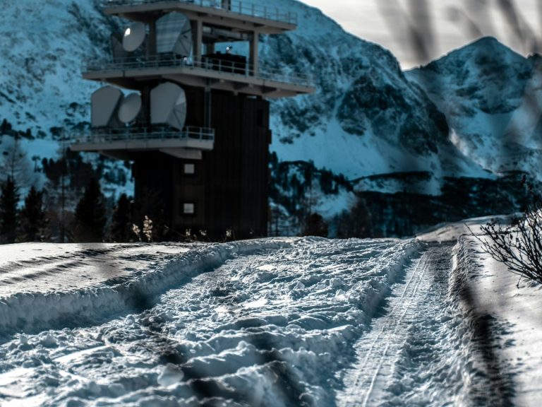 Snow-covered landscape with a tall structure and mountains in the background.