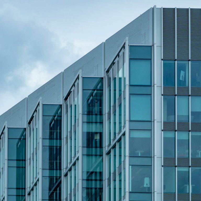 Modern glass building with angular design and cloudy sky in the background.
