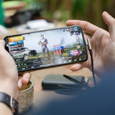Person holding a smartphone, playing a mobile game in an outdoor setting.