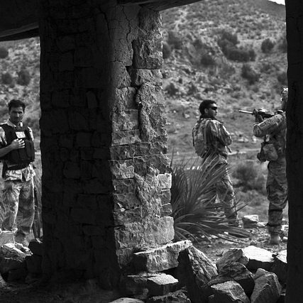 Three soldiers in an arid landscape, framed by a rustic stone structure.