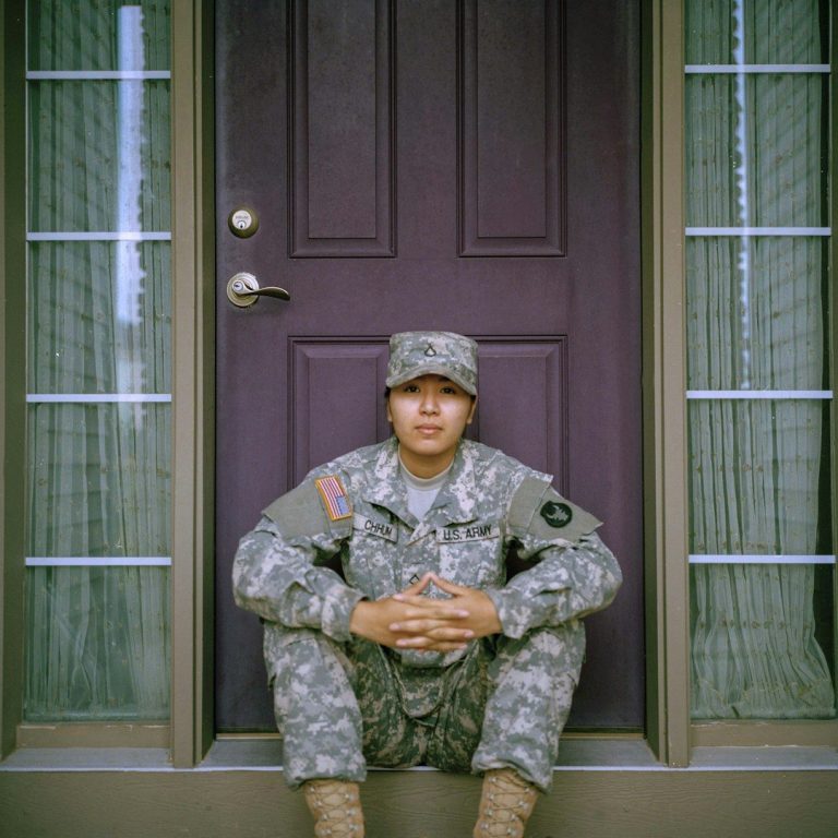 A soldier in uniform sitting on the steps in front of a door.