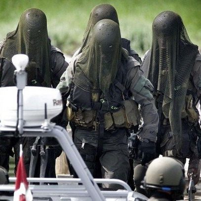 Four masked individuals in tactical gear approach a boat, wearing netting over their heads.