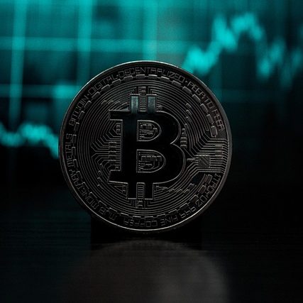 Bitcoin coin in front of a teal and black financial graph backdrop.